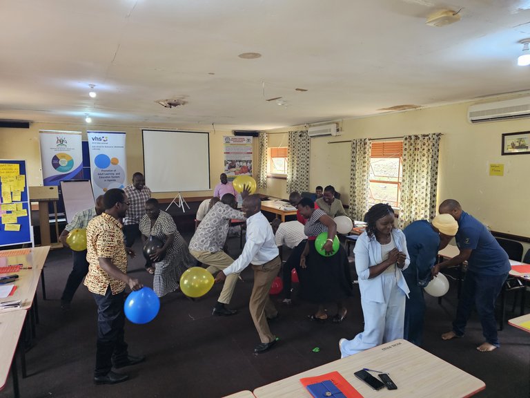 A group of people are mingling in a room, they are holding balloons and appear to be running with them.