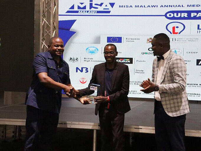Drei Männer auf einer Bühne bei der MISA Malawi Annual Media Awards, einer übergibt einen Preis an einen anderen, der dritte klatscht Beifall