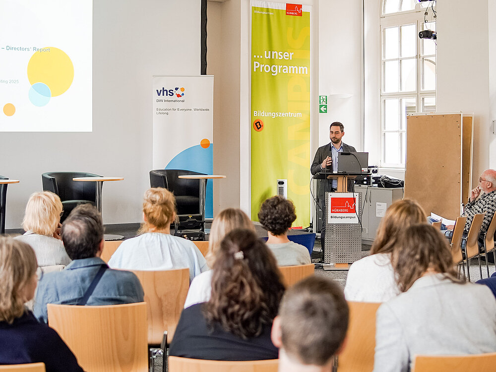 Ein Mann steht am Rednerpult und spricht vor einer Gruppe Menschen.