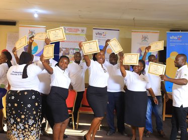 A group of people are standing together in a room, holding their certificates up in the air.
