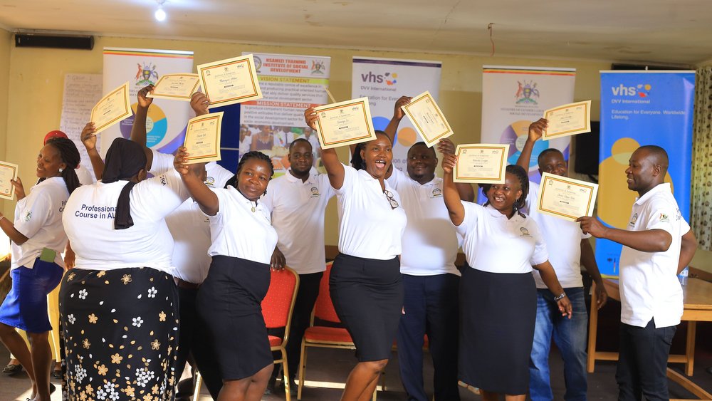 A group of people are standing together in a room, holding their certificates up in the air.