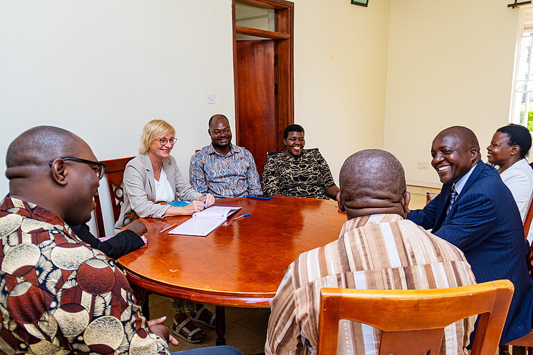 Eight people are seated around a round table. They appear to be talking and smiling. 