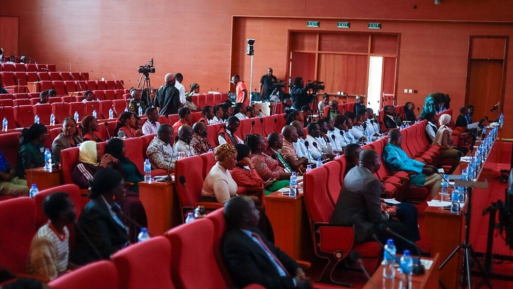 A group of people is seated in rows of chairs, facing forward.