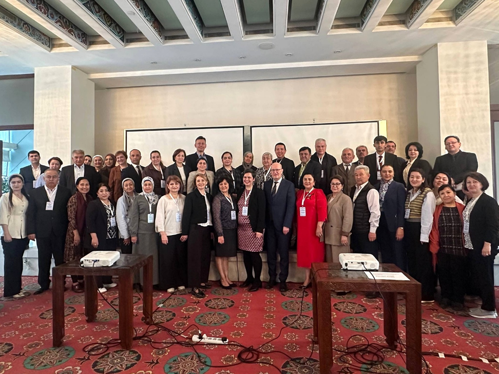 Group photo of around 40 people in a conference hall. Most people are wearing business or smart-casual attire and conference name badges.