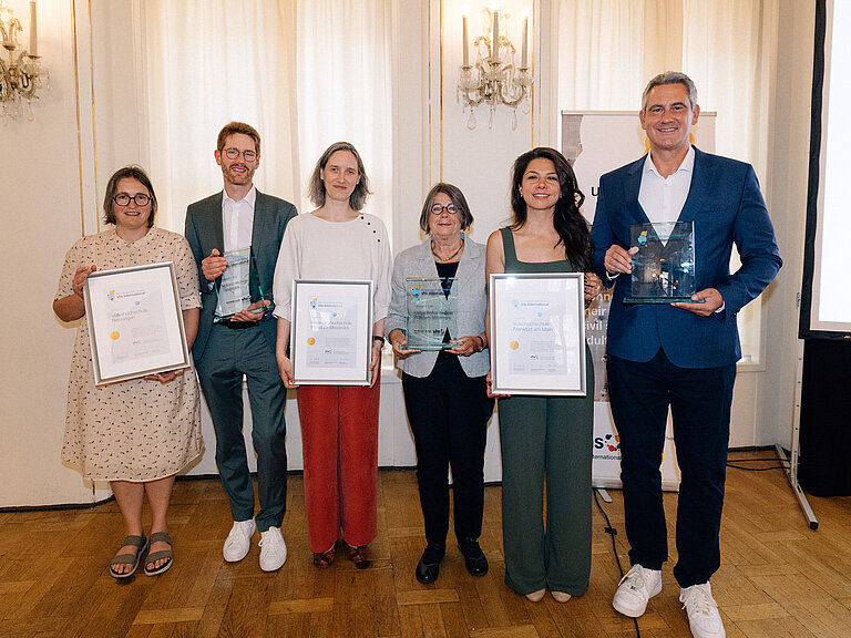 Die PreisträgerInnen stehen in einer Reihe nebeneinander und halten ihre Urkunden und Auszeichnungen in den Händen.