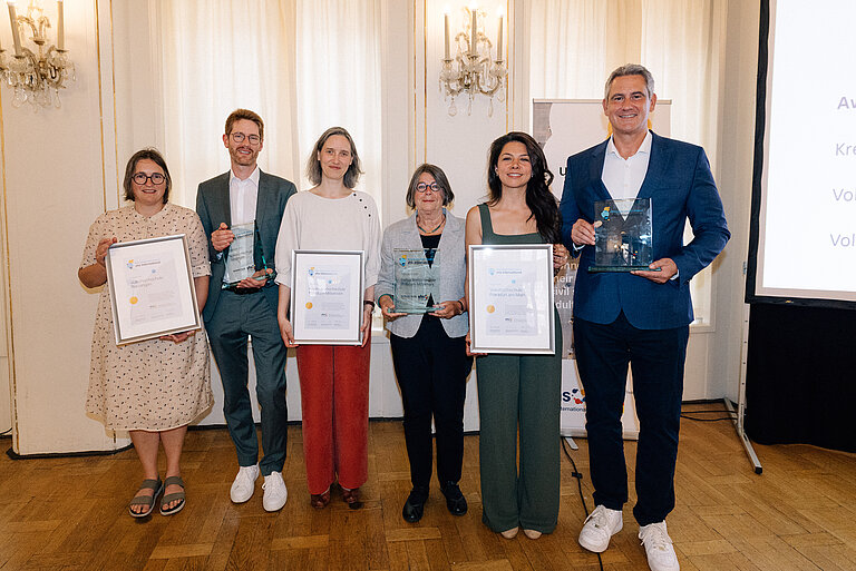 Alle PreisträgerInnen stehen nebeneinander und halten ihre Auszeichnungen und Urkunden in den Händen.