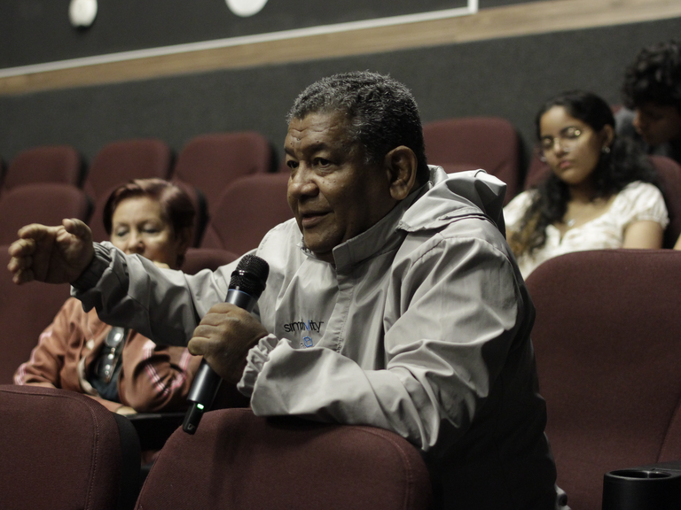 A man sits in a cinema auditorium and speaks into a microphone.