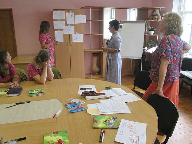 Women standing in a room and analyising pictures.